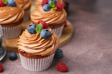Tasty cupcakes with chocolate cream and berries on brown table, closeup. Space for text