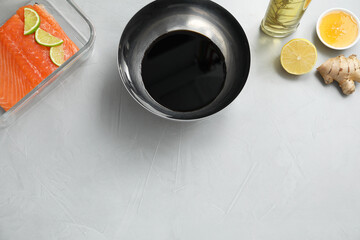 Soy sauce in bowl, salmon fillet, oil, honey, lemon and ginger on gray textured table, flat lay. Space for text