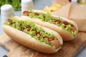 Tasty hot dogs with lettuce, ketchup and potato fries on light grey table, closeup