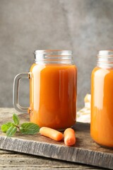 Fresh carrot juice in mason jars, vegetables and mint on wooden table against gray background