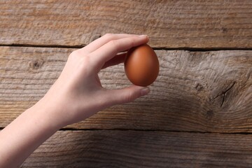 Woman with raw egg at wooden table, top view