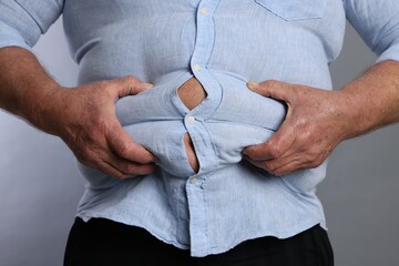 Overweight man in tight shirt on grey background, closeup