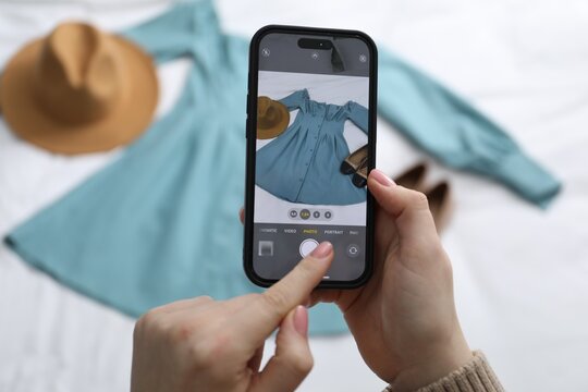 Woman with smartphone taking photo of her used clothes indoors, selective focus