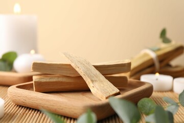 Palo santo sticks, eucalyptus branches and burning candles on bamboo mat, closeup