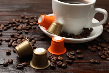 Coffee capsules, cup of hot drink and beans on wooden table, closeup
