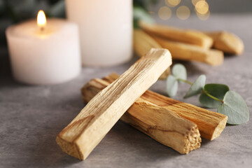 Palo santo sticks, eucalyptus branch and burning candles on grey table, closeup