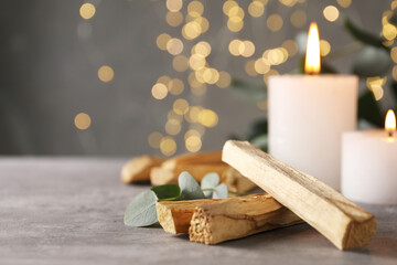 Palo santo sticks, eucalyptus branch and burning candles on grey table, closeup. Space for text