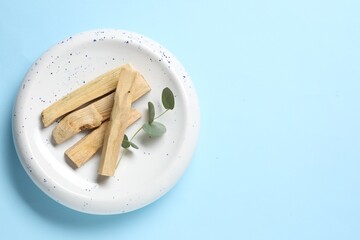Palo santo sticks and eucalyptus branch on light blue background, top view. Space for text