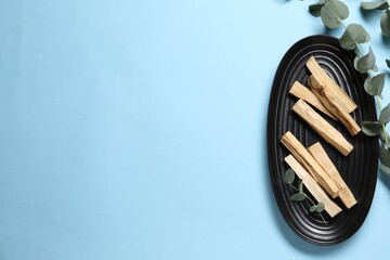 Fototapeta premium Palo santo sticks and eucalyptus branches on light blue background, flat lay. Space for text