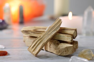Palo santo sticks, gemstones and burning candle on white wooden table, closeup