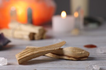 Palo santo sticks, gemstones and burning candle on white wooden table, closeup