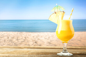 Tasty pineapple cocktail in glass on wooden table against seascape. Space for text