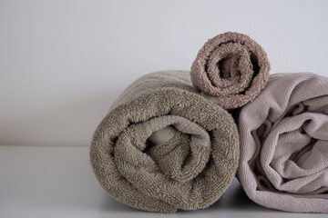 A neat stack of three rolled towels in neutral tones, including the Pantone Color of the Year 2025, Mocha Mousse, displayed on a clean white surface