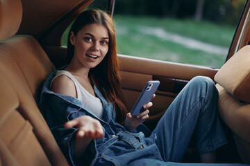 Young woman sitting in a car with a smartphone, expressing surprise, casual style, denim outfit,...