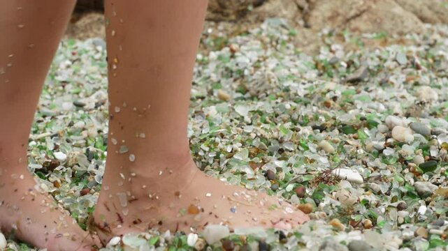 Barefoot walking on smooth sea glass covered shoreline, revealing colorful coastal landscape at scenic beach destination