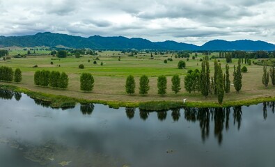 Aerial view of a tranquil rural landscape. A calm lake reflects the surrounding trees and fields. Birds are visible on the water. LAKE ANIWHENUA, MURUPARA, BAY OF PLENTY, NEW ZEALAND