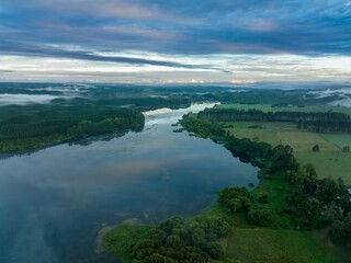 Misty morning over a tranquil Lake Aniwhenua. Reflecting clouds, lush forests, and farmland. Aerial view.  MURUPARA, BAY OF PLENTY, NEW ZEALAND