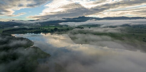 Misty morning over a tranquil lake. Reflections of clouds on still water. Peaceful rural landscape. LAKE ANIWHENUA, MURUPARA, BAY OF PLENTY, NEW ZEALAND