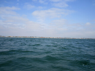 Photo of water from the sea, small waves. The sea coast is visible on the horizon.