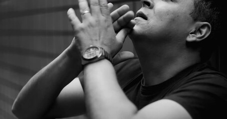 Distressed man looking up with clasped hands, desperate for hope, struggling with emotional crisis, mental illness, depression, despair, inner turmoil, monochrome drama