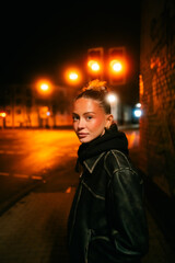 Portrait of a stylish young woman in a black leather jacket at night, illuminated by warm urban streetlights, creating a cinematic and moody atmosphere.