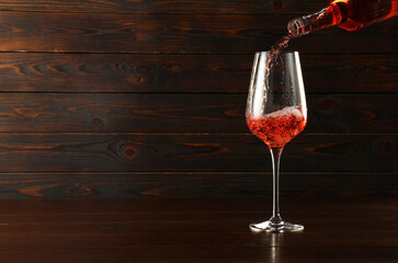Pouring rose wine into glass at wooden table, space for text