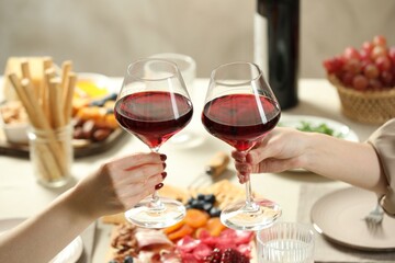Women clinking glasses of wine during dinner at table indoors, closeup