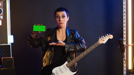 Cool rebellious rock star does a live performance pointing to copy space screen at nightclub, feeling powerful in her leather jacket and dark make up. Trendy powerful girl performing. Camera A.