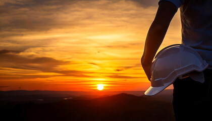 Silhouette of a person holding a hard hat at sunset.  Dramatic imagery ideal for construction, engineering, safety, and achievement themes.  Perfect for websites, articles, or social media.