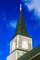 A church steeple with a green roof and a white cross on top