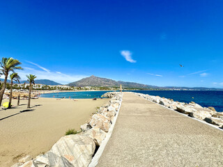 Fototapeta premium Playa Puerto Banús beach with palms and a view towards the Pico de la Concha mountain seen from the view from the harbor wall, landmark of Marbella, Malaga, Costa del Sol, Spain