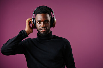Young Black man wearing headphones, posing confidently against a vibrant purple background, conveying a modern lifestyle and passion for music