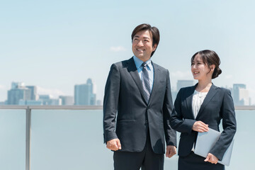 都会で働くパソコンを持ったスーツ姿の男女（ビジネスマン）
