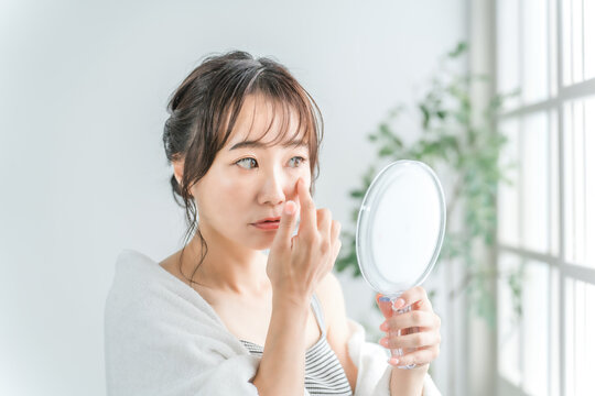 部屋で鏡を使い目・目元を見るアジア人女性

