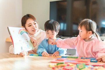 Fototapeta premium 保育園・幼稚園・託児所・保育所で園児に紙芝居・絵本を読み聞かせする女性保育士・保母さん・シッター 