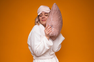 A woman in white robe and pink sleep mask, gently hugging soft pink pillow, with a content...