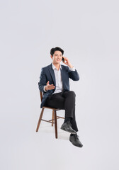 Full body image of young Asian business man using phone and sitting in chair on white background