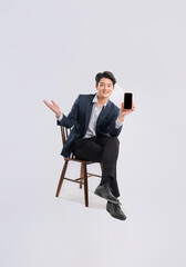 Full body image of young Asian business man using phone and sitting in chair on white background