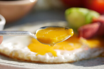 CloseUp of a Spoon with a Runny Egg Yolk on Fried Egg Whites, a tasty and healthy breakfast