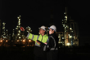 Obraz premium Male and female chemical engineers working with laptops of gas refinery plant and refinery oil factory industry at night
