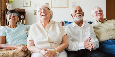 Group of four elderly people sitting on a couch, smiling and laughing. Diverse group enjoying time together in a cozy living room setting. Elderly people laughing together in retirement home.