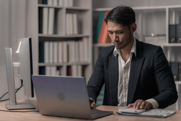 Fototapeta premium Businessman analyzes market research on his laptop and computer To maintain productivity and quality, young designer works late into the night using a laptop in the office.