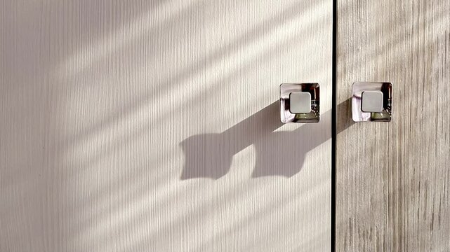 Furniture silver handles on structural laminated chipboard facades doors in striped shadows from sunlight close-up. Furniture fittings.
