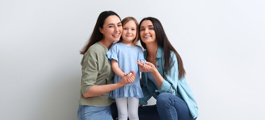 Fototapeta premium Young lesbian couple with adopted little girl on light background
