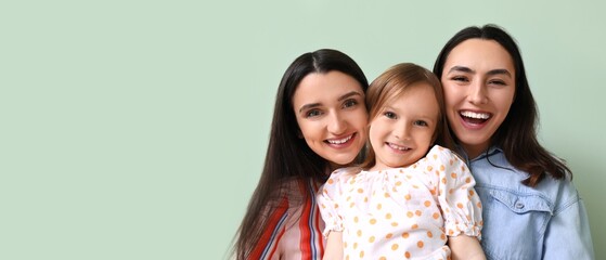 Young lesbian couple and adopted little girl on green background with space for text