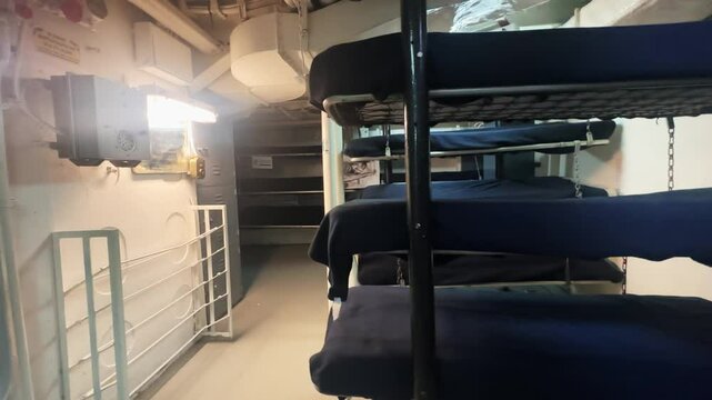Bunk beds in a military ship's compact sleeping quarters with industrial lighting