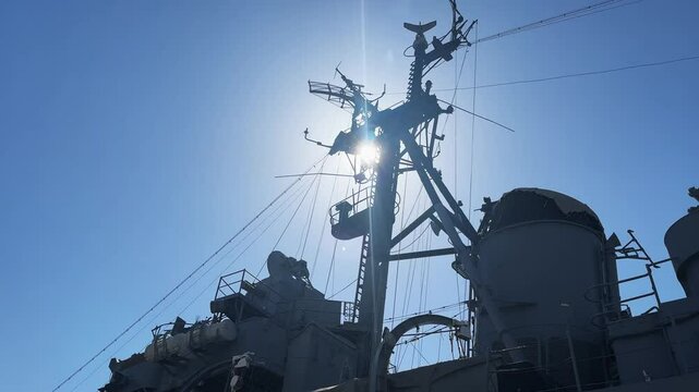 Silhouette of a military naval ship's radar and communication equipment, framed against a bright blue sky, highlighting robust and intricate technology
