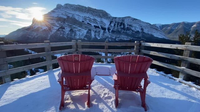 Banff Alberta Canada, January 06 2025: Slow motion sunrise behind Canadian Rockies tracking shot over viewpoint chairs.
