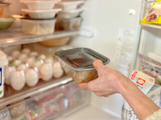 冷蔵庫に密閉容器を入れる高齢女性の手元