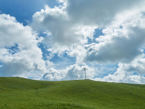 Rolling green hills under a bright, partly cloudy sky. A lone communication tower stands atop a hill. - Powered by Adobe